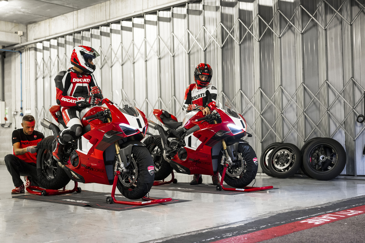 Dois pilotos em suas motos Ducati Panigale vermelho e branca, parados em um galpão